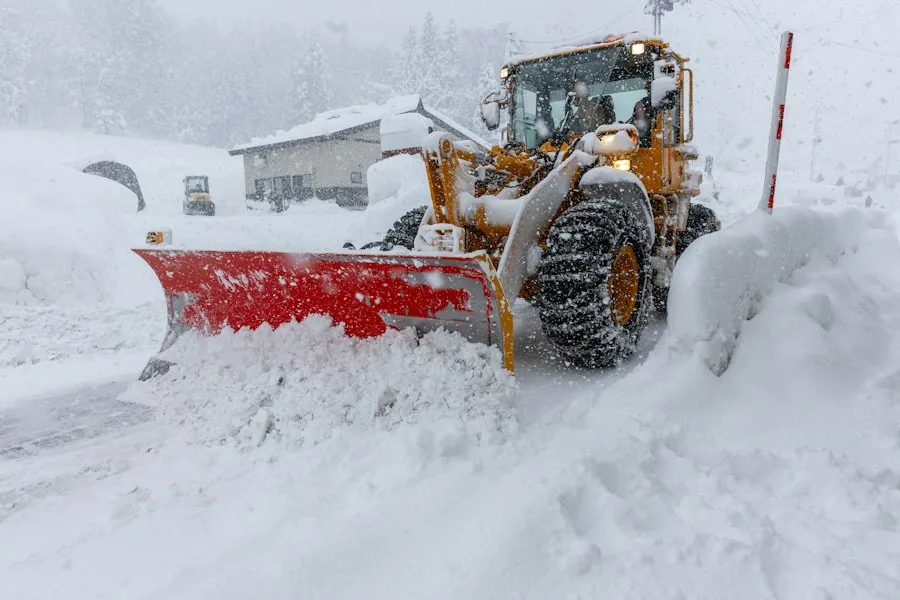 A loader with a red plow blade clearing deep snow